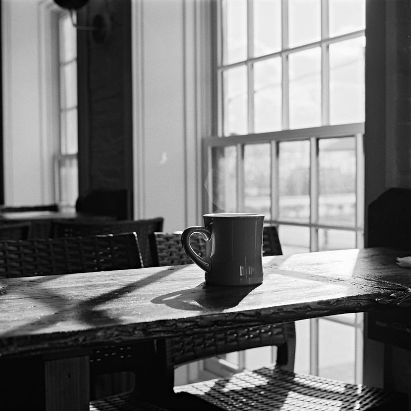 A steaming coffee cup sitting on a sunlit table.